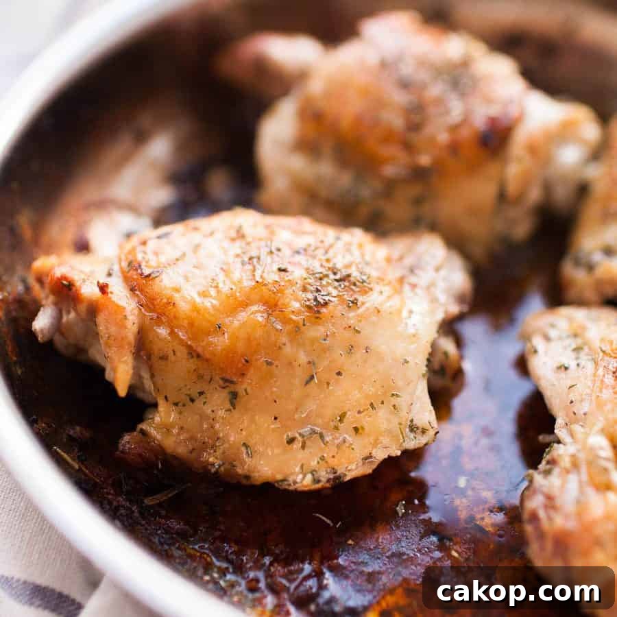 A close-up of pan seared chicken thighs in a pan, with a golden-brown crispy skin and herbs sprinkled on top.