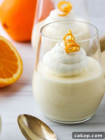 Light and Creamy Orange Mousse in a a glass next to a spoon and an orange.
