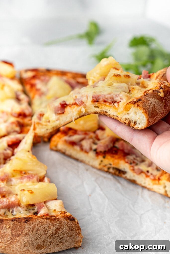 A piece of ham and pineapple pizza being picked up.