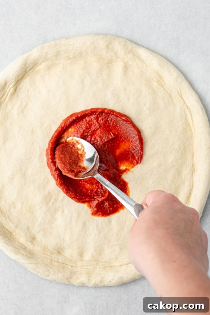 Spooning sauce onto the stretched pizza base.