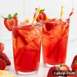 Two tall glasses of strawberry sweet tea with garnishes of fresh lemon and strawberries, surrounded by ingredients.