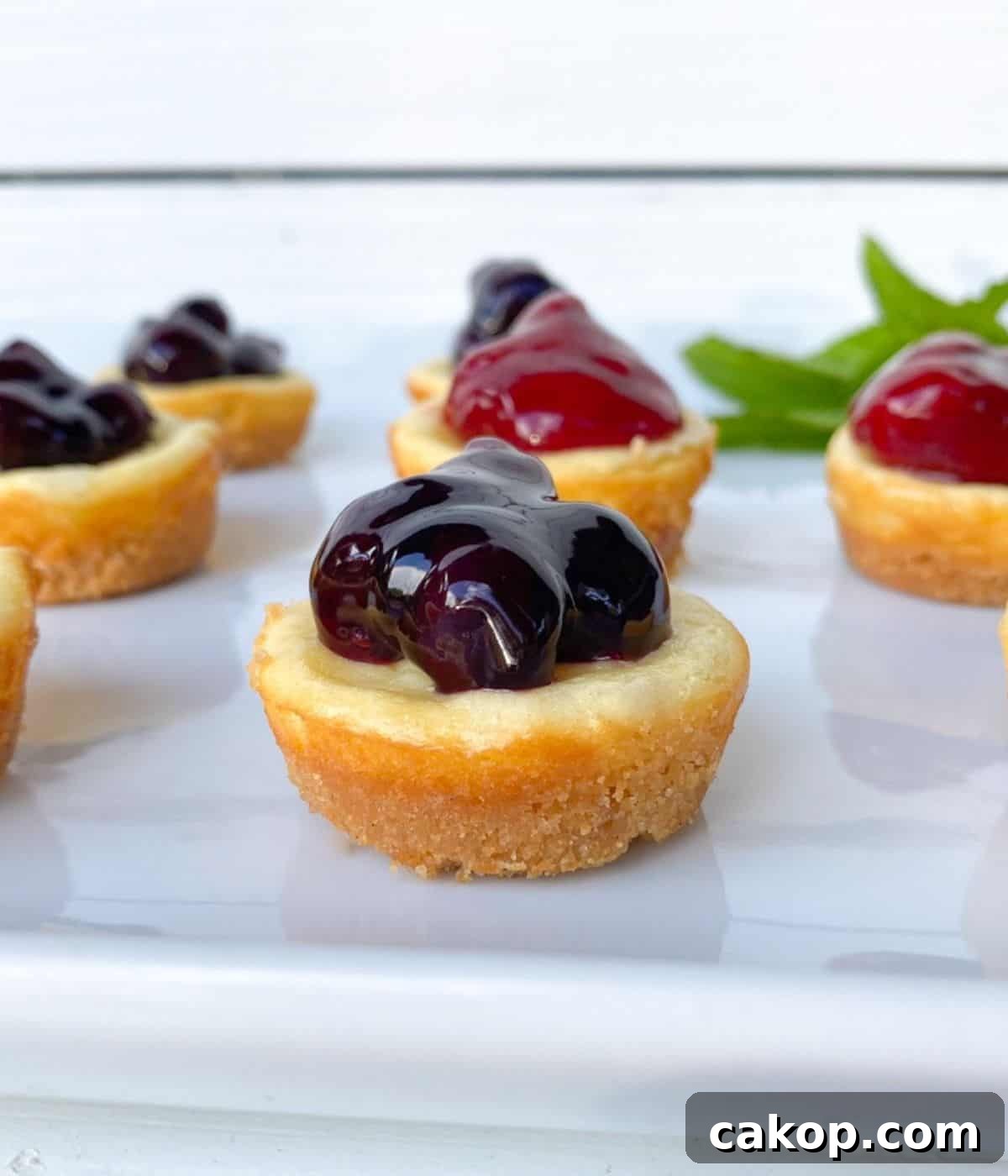 Mini Cheesecakes with Cookie Crust — Irresistible Bite-Sized Treats 2 mini plain cheesecakes on a white plate topped with strawberries and blueberries.