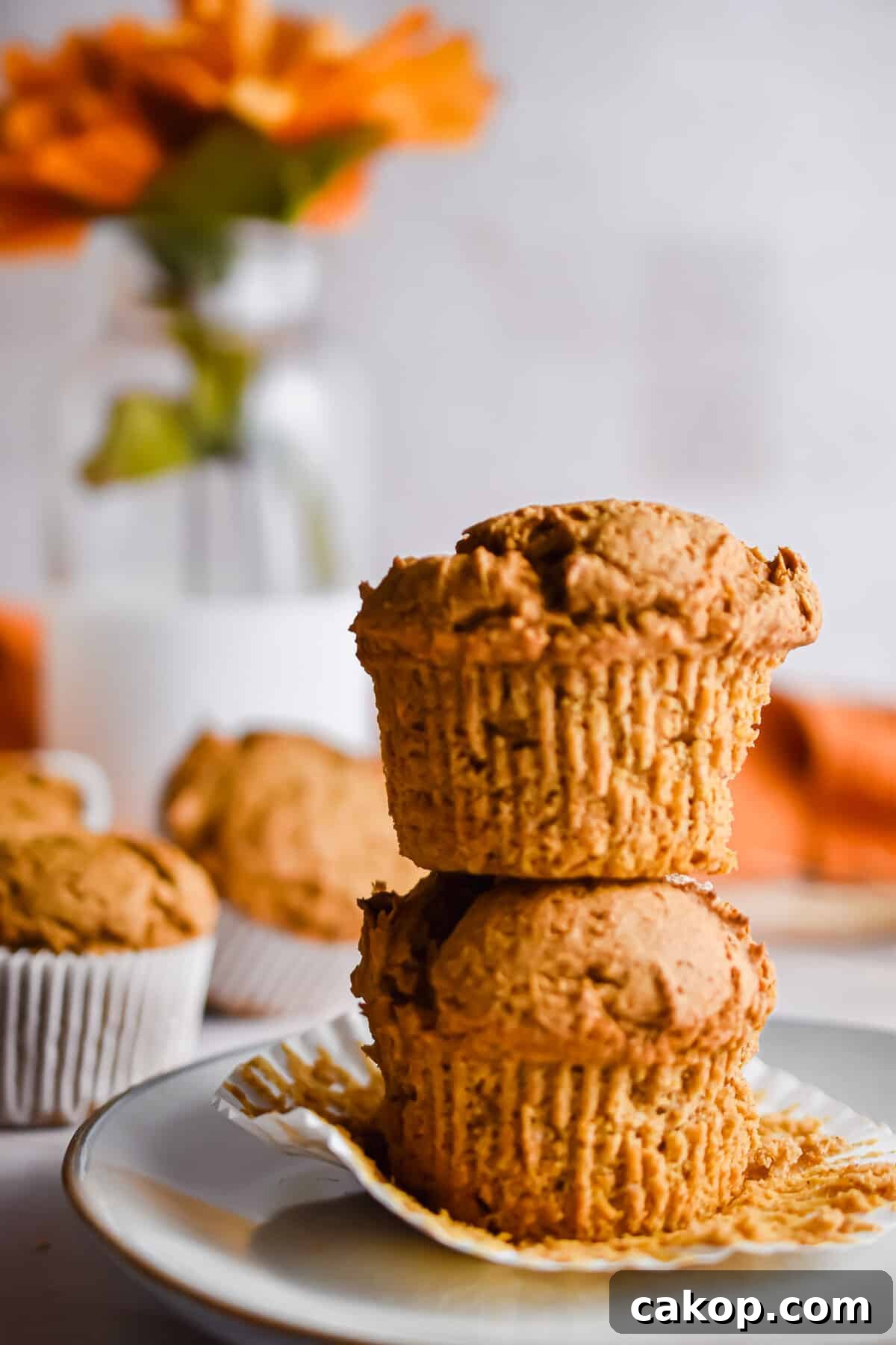 2-Ingredient Pumpkin Spice Muffins — Quick Autumn Recipe 9 Two muffins are on top of one another with flowers in the background.