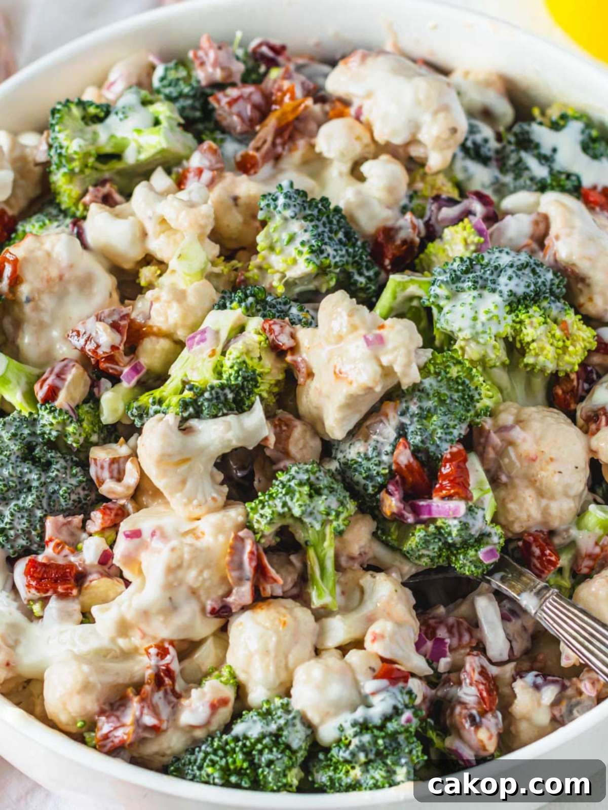 Healthy broccoli cauliflower salad with Greek yogurt dressing close up in a white bowl.