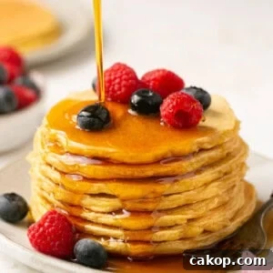 protein pancakes stacked on a plate with berries and maple syrup being poured on top