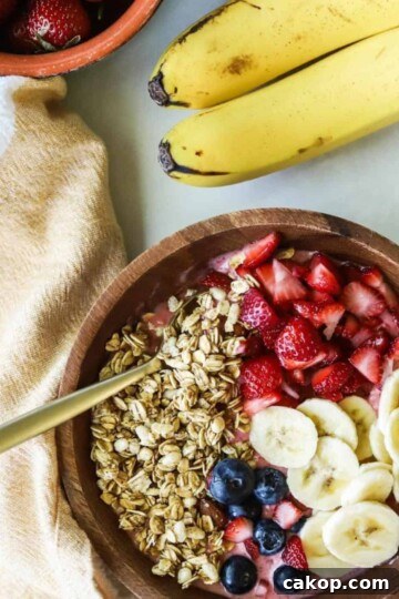 Strawberry banana smoothie bowl in wooden bowl topped with granola, banana, strawberries and blueberries.