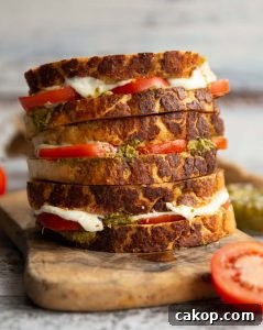 3 sandwiches stacked on each other with tomato, mozzarella and pesto spilling out