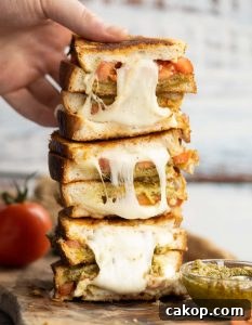 4 sandwich halves stack on each other on wooden board with hand grabbing the top one