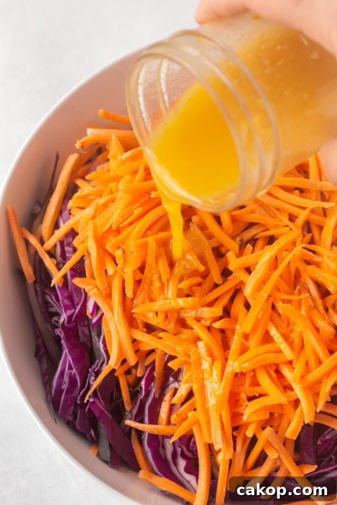 What to Serve with Coleslaw: 25+ Delicious Meal Ideas 4 Pouring orange vinaigrette dressing into a white bowl filled with thinly sliced purple cabbage and carrot matchsticks.