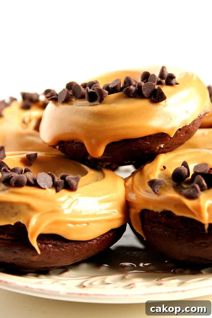 Side shot of three chocolate donuts with peanut butter glaze and chocolate chips, stacked up on each other. 