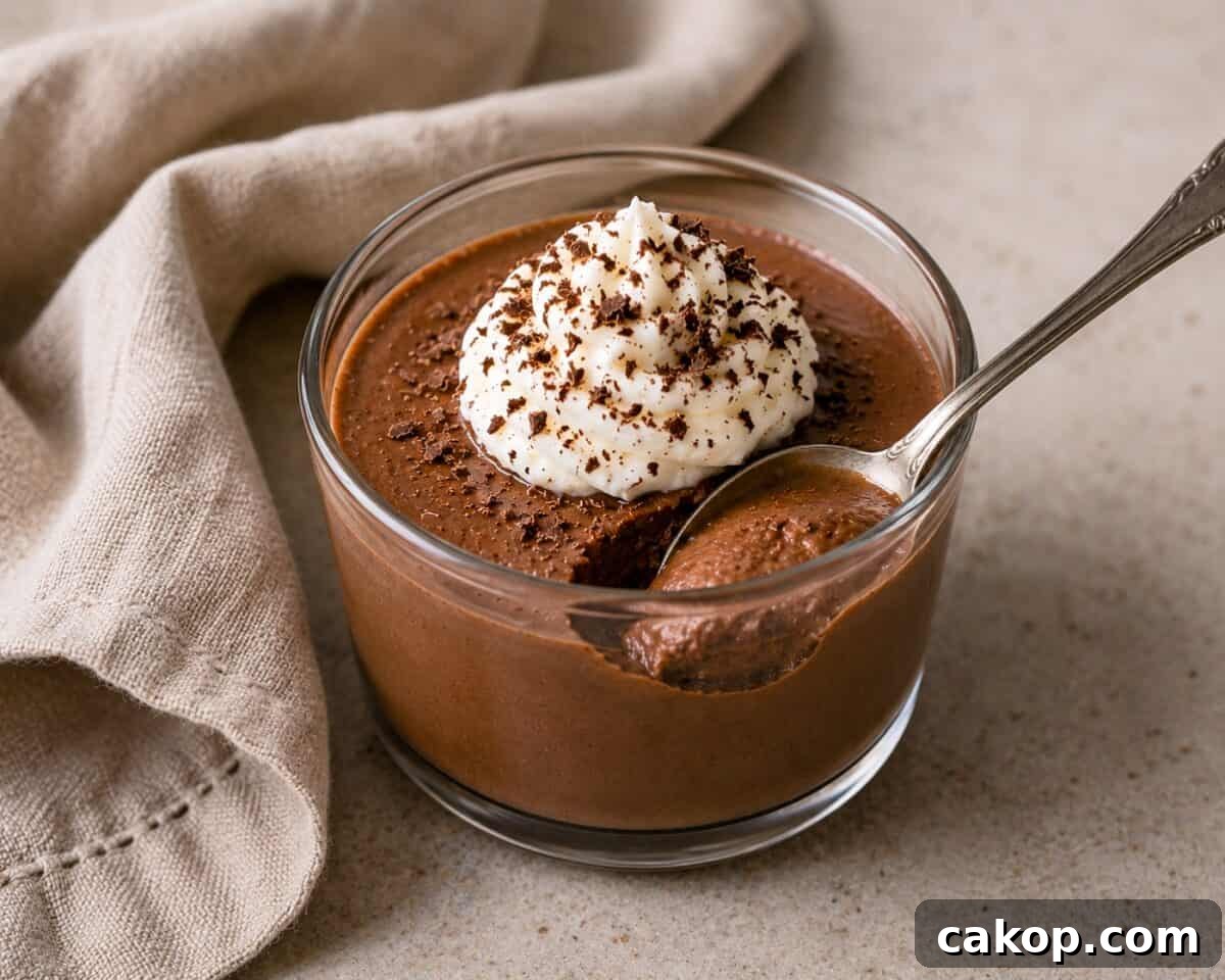 Mocha Pots de Creme topped with whipped cream and chocolate shavings in dessert glass with a spoon and a linen napkin alongside.
