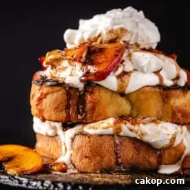 Pound cake slices topped with cream and peach slices on a black plate.