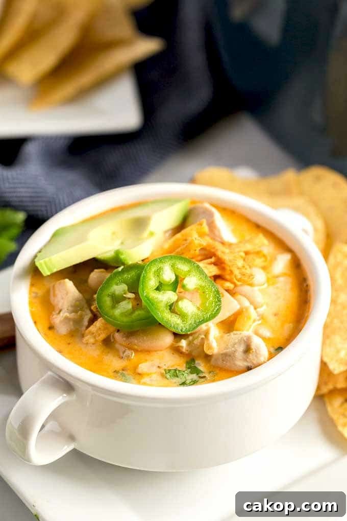 White Chicken Chili served in a white bowl and topped with cheese, tortilla chips and jalapenos.