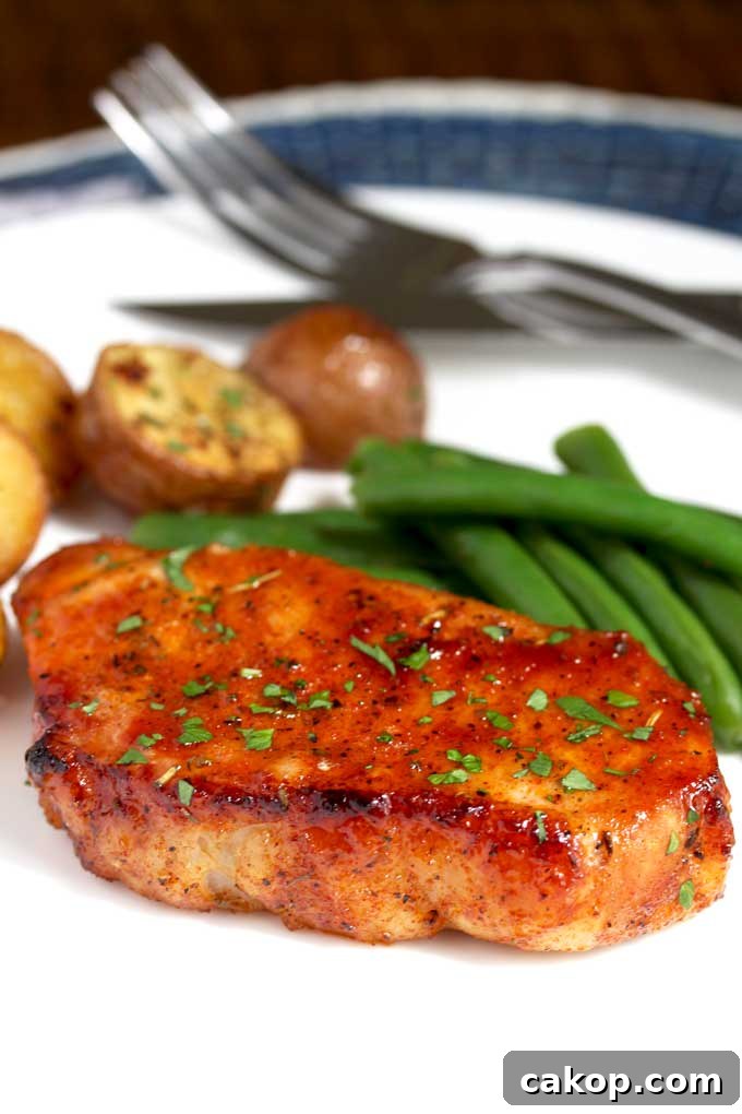An oven baked pork chop on a white plate with roasted potatoes and green beans.