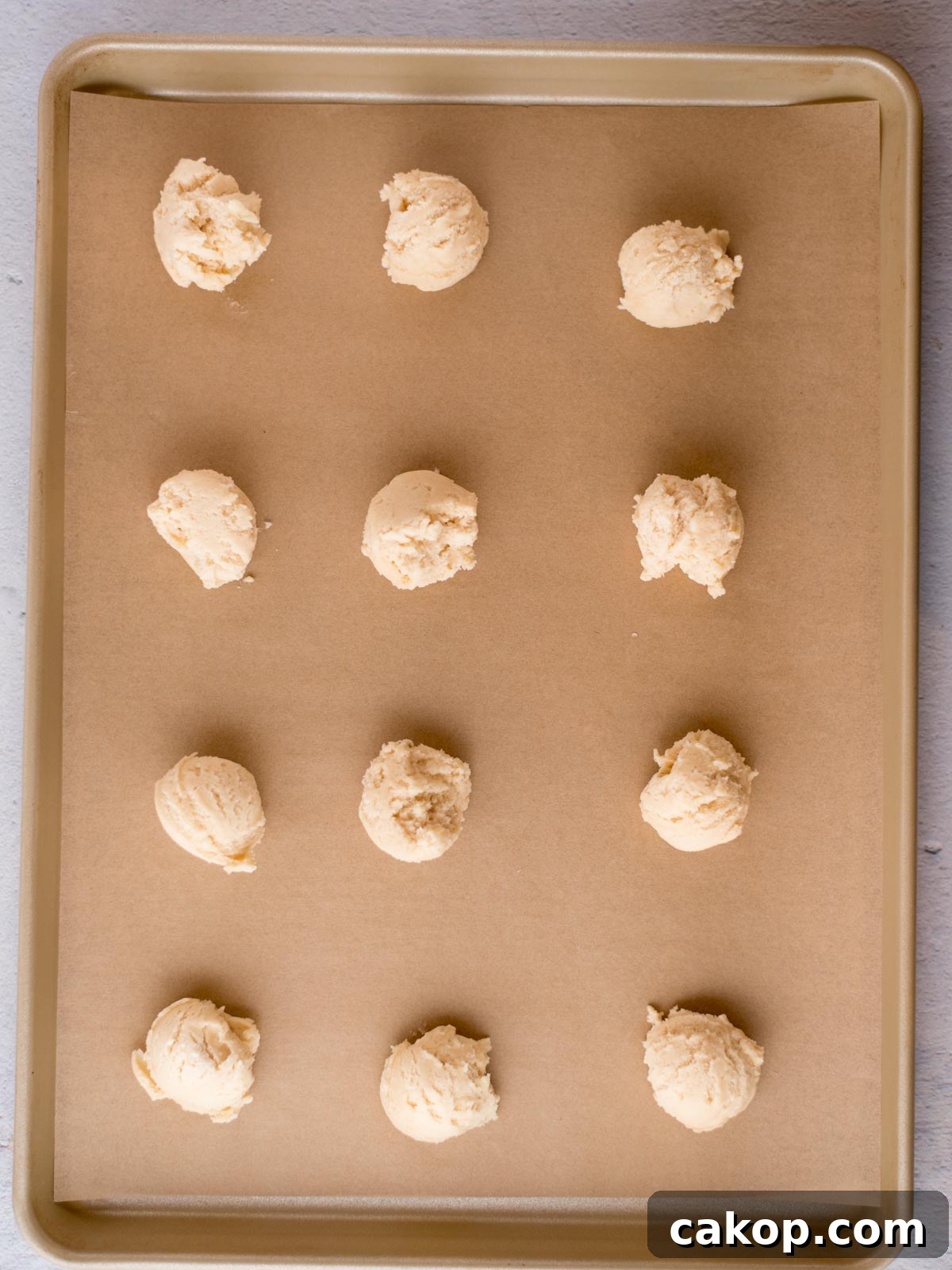 scooped balls of condensed milk cookie dough on a parchment lined baking sheet