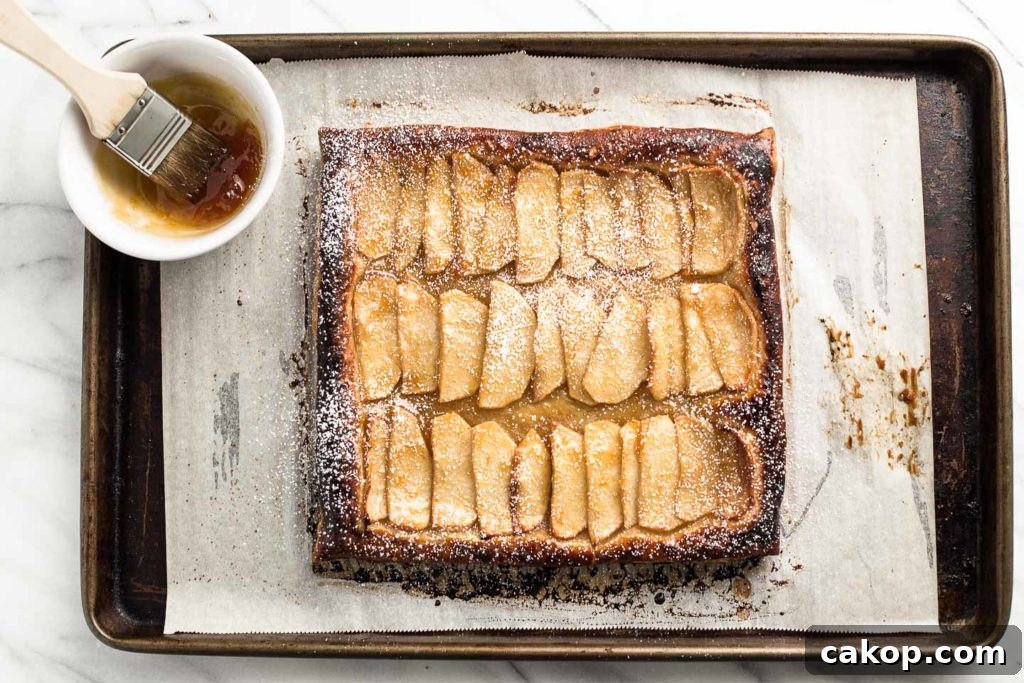 How to Make a Rustic Apple Tart: Flaky Crust & Cinnamon Apples 3 apple tart on a baking sheet with apricot jam in a bowl.