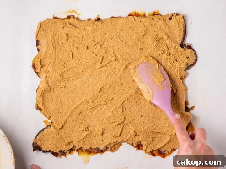 High-Protein Snickers Date Bark Recipe for Satisfying Snacks 12 Peanut butter mixture being spread over the flattened date layer with a pink spatula