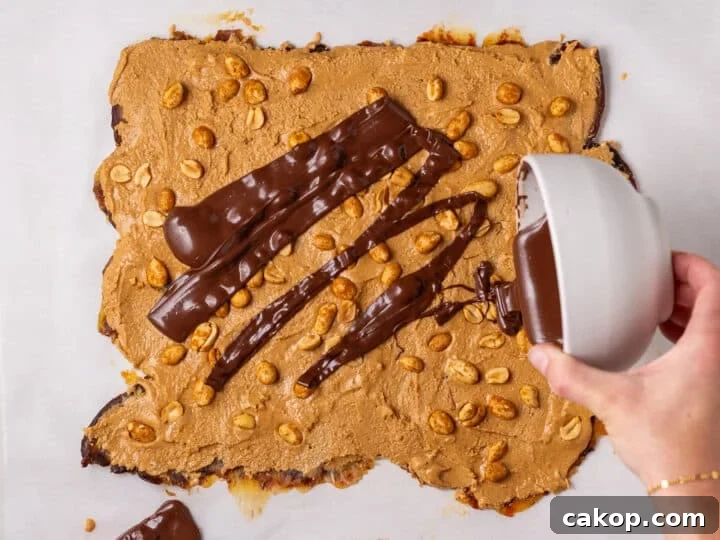 High-Protein Snickers Date Bark Recipe for Satisfying Snacks 14 Melted chocolate being poured over the peanut butter and peanut layer