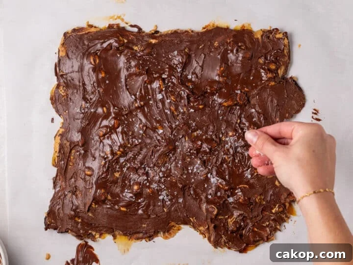 High-Protein Snickers Date Bark Recipe for Satisfying Snacks 16 Flaky sea salt being sprinkled over the melted chocolate layer