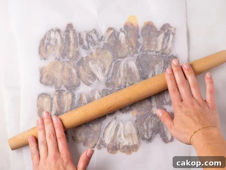 High-Protein Snickers Date Bark Recipe for Satisfying Snacks 8 A rolling pin flattening dates between two sheets of parchment paper