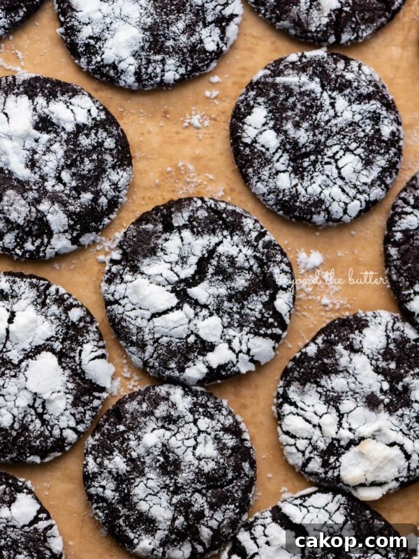 Chocolate Pinwheel Cookies Recipe — Swirled Cocoa Butter Cookies 9 Just baked dark chocolate crinkle cookies on a brown parchment paper lined baking sheet.
