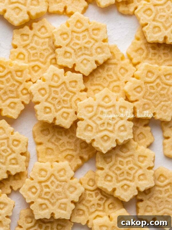 Chocolate Pinwheel Cookies Recipe — Swirled Cocoa Butter Cookies 10 Butter cookies shaped as snowflakes randomly placed on a white parchment paper lined baking sheet.
