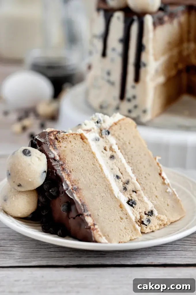A cookie dough cake covered in cream cheese cookie dough frosting with dark brown chocolate ganache drip and topped with edible cookie dough balls.