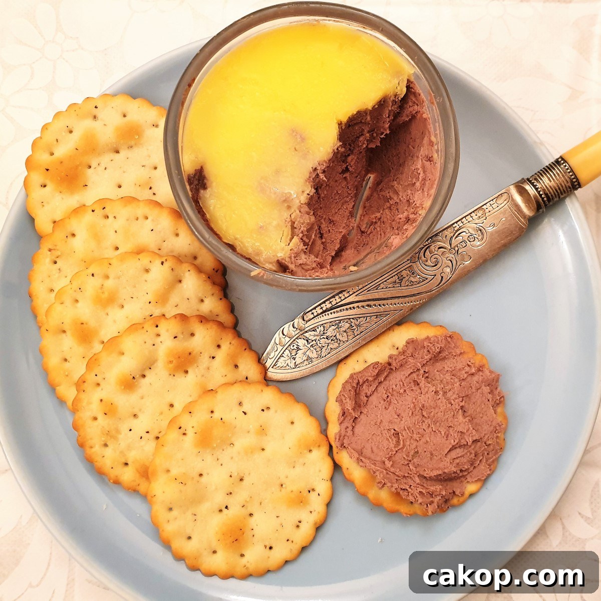 A dish of chicken liver pate on a plate with a biscuit spread with the pate.