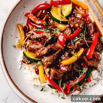 Beef stir fry with Asian sauce and peppers with rice in a bowl.