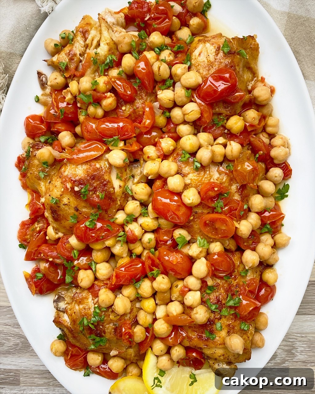 Slow Cooker Chicken with Chickpeas and Tomatoes Recipe 2 overhead shot of cooked crockpot chicken chickpeas tomatoes on a white plate garnished with fresh parsley
