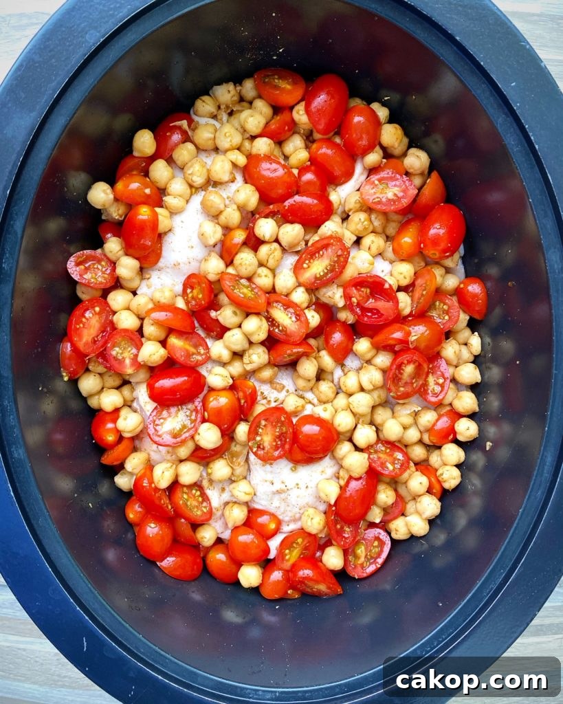 overhead shot of uncooked crockpot chicken chickpeas tomatoes in a black slow cooker
