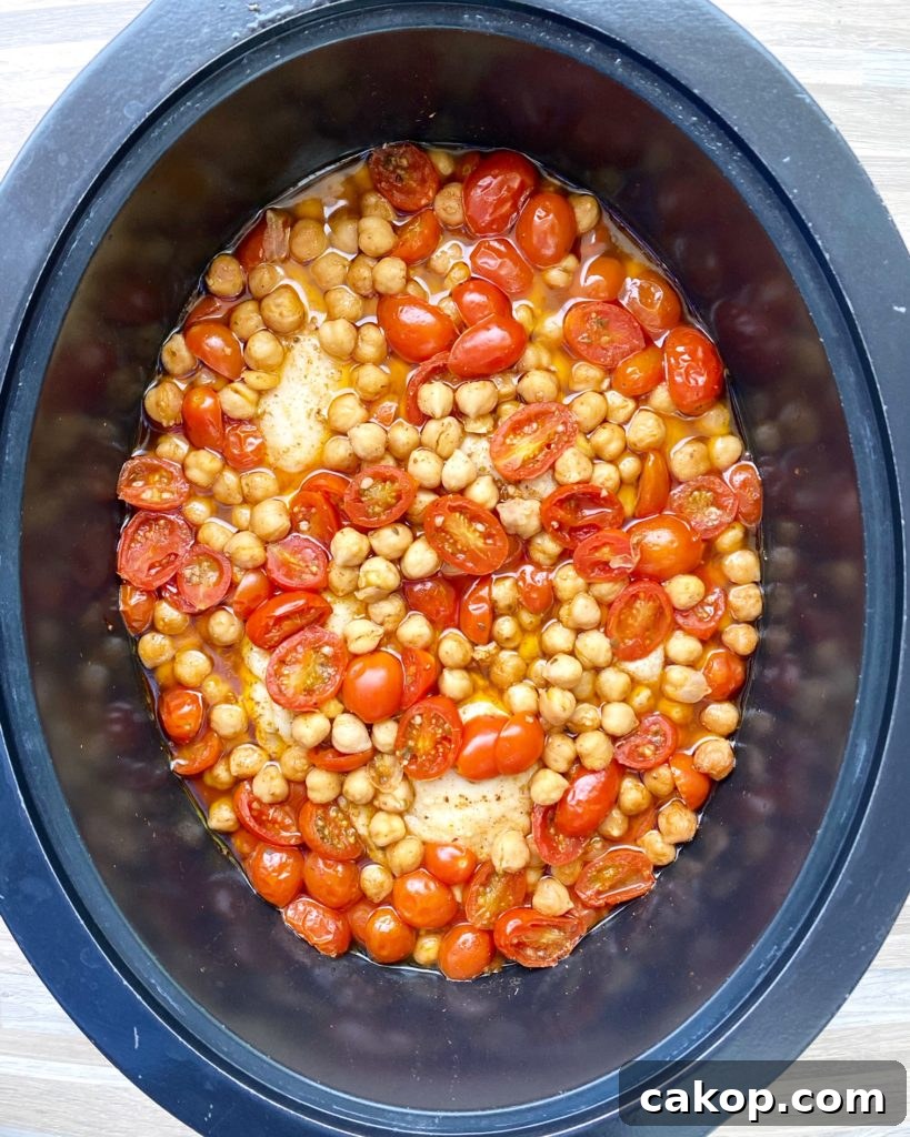 overhead shot of cooked crockpot chicken chickpeas tomatoes in a black slow cooker