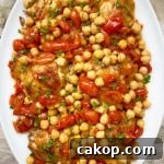 overhead shot of cooked crockpot chicken chickpeas tomatoes on a white plate garnished with fresh parsley