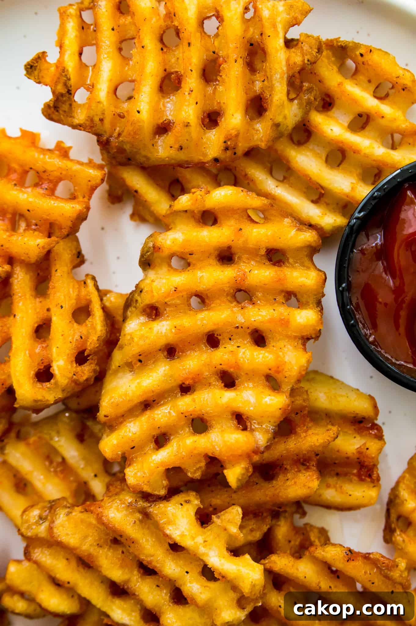 A plate of cooked waffle fries with ketchup A plate of cooked waffle fries with ketchup beside the fries.