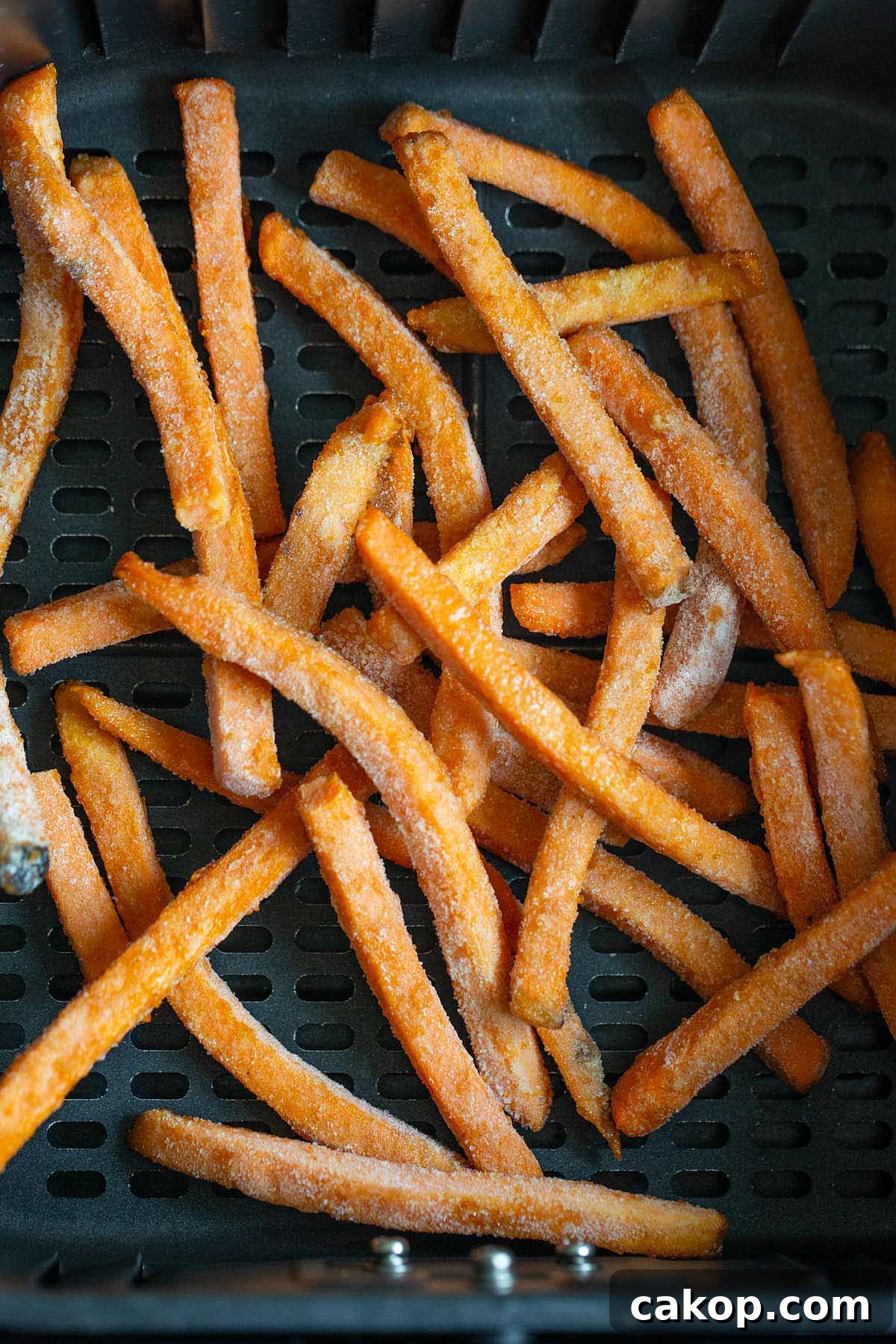 Frozen sweet potato fries in air fryer basket.