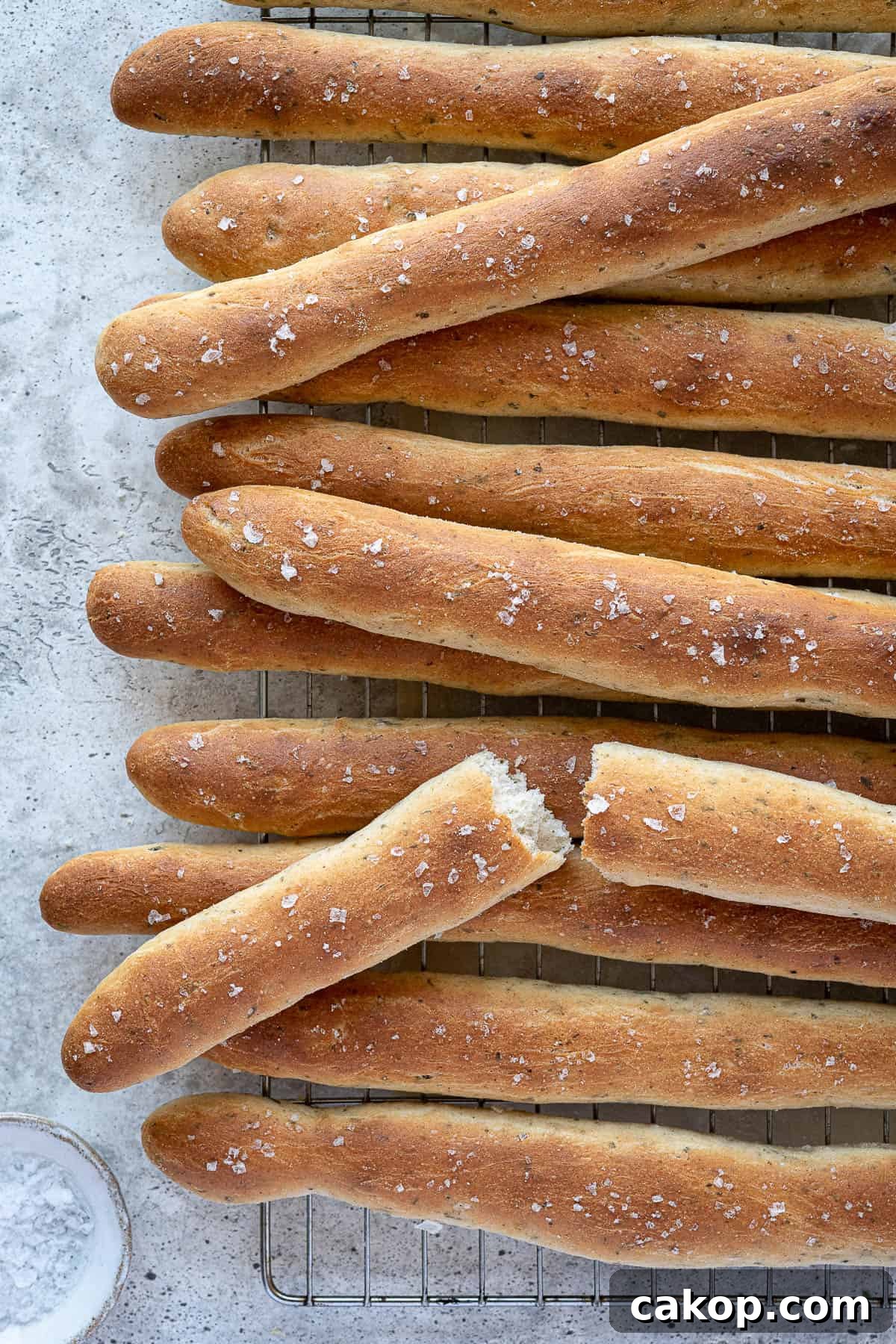Breadsticks on a wire rack, one broken in half.