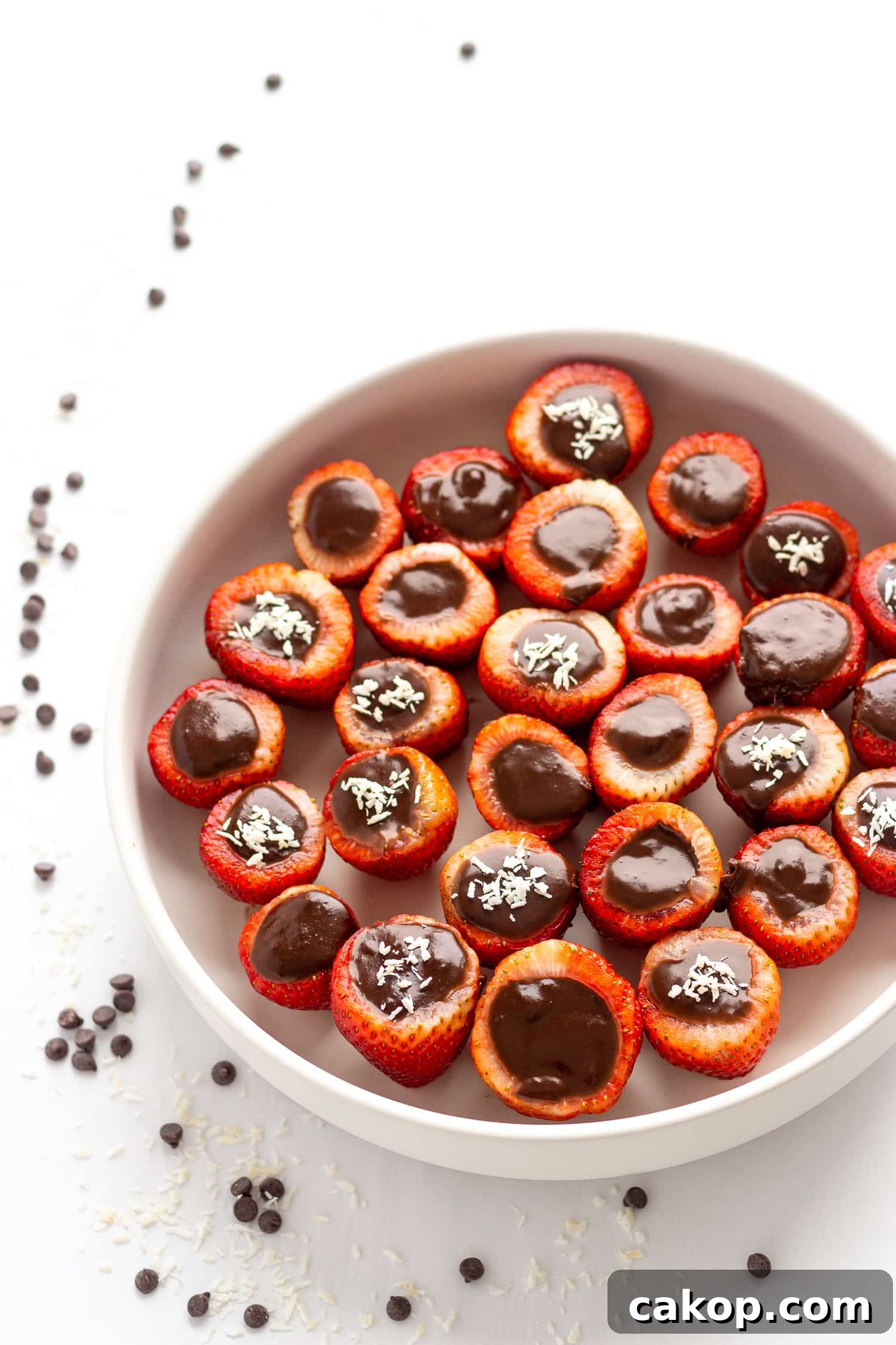 White bowl filled with chocolate coconut cream stuffed strawberries.  Set on a white background with a scattering of chocolate chips and shredded coconut.