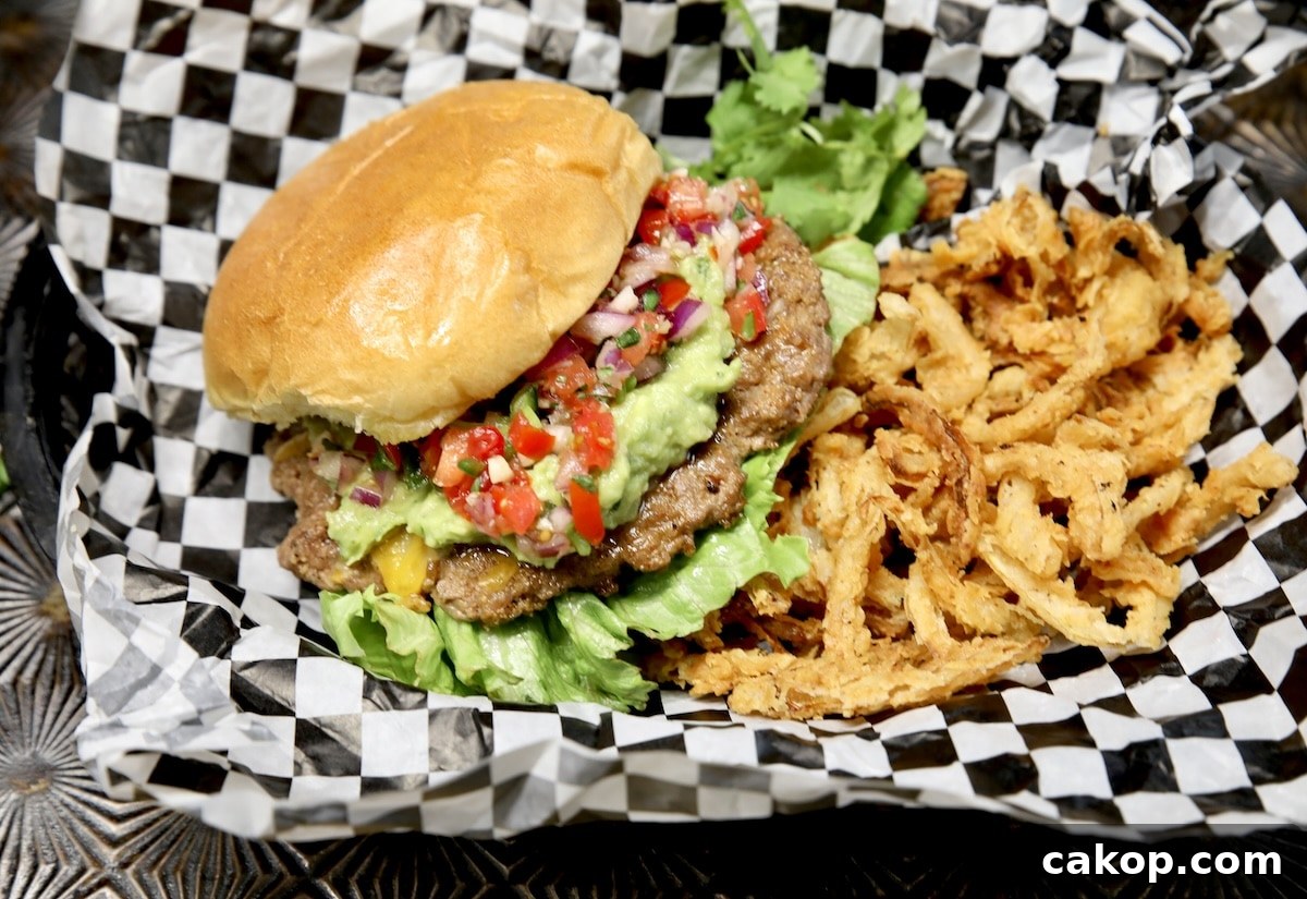 Burgers with guacamole and pico de gallo. Burger with guacamole and salsa with onion strings on black and white checked paper.