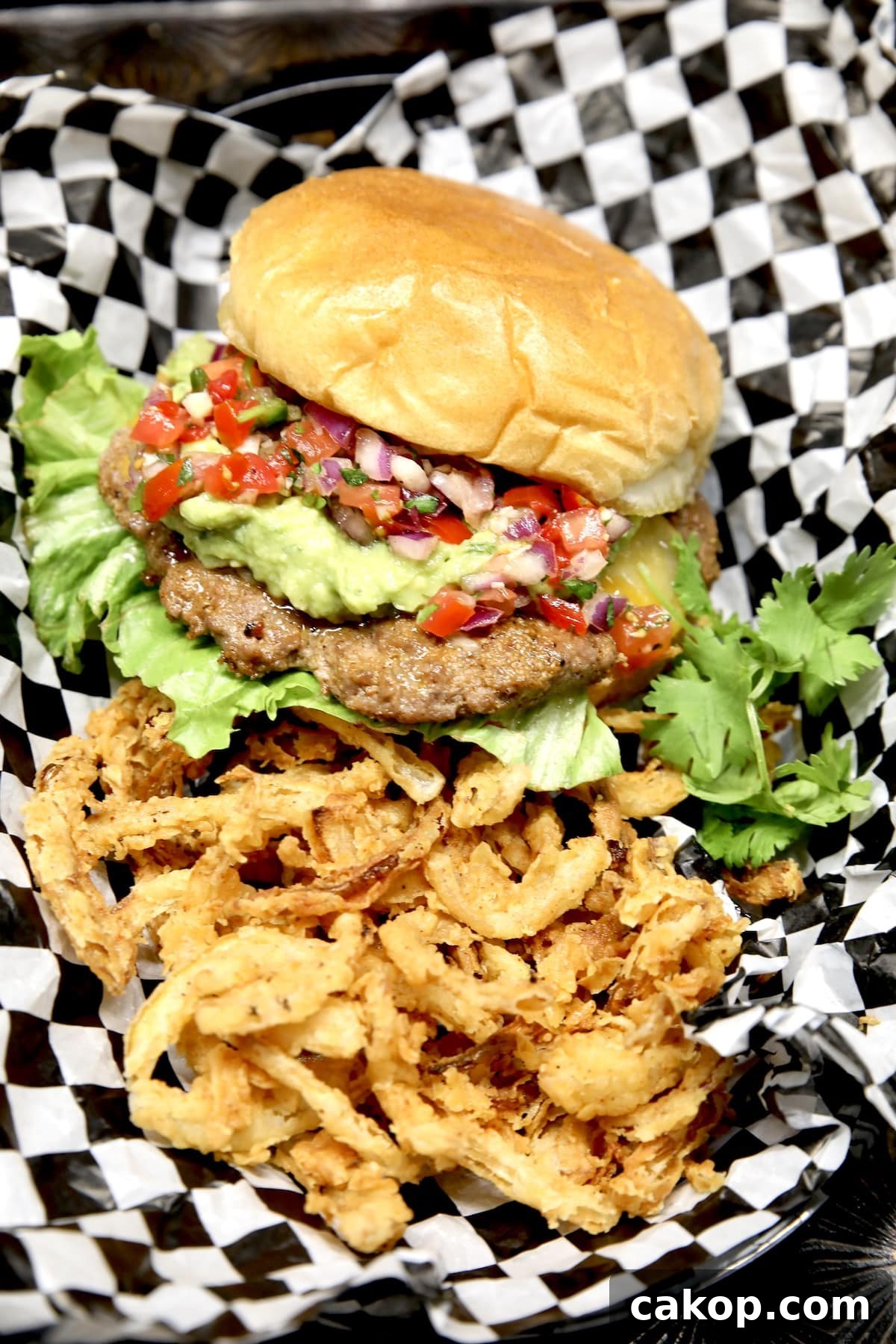 Smash burgers with guacamole and pico de gallo. Guacamole burger with onion strings in diner basket with checked paper.