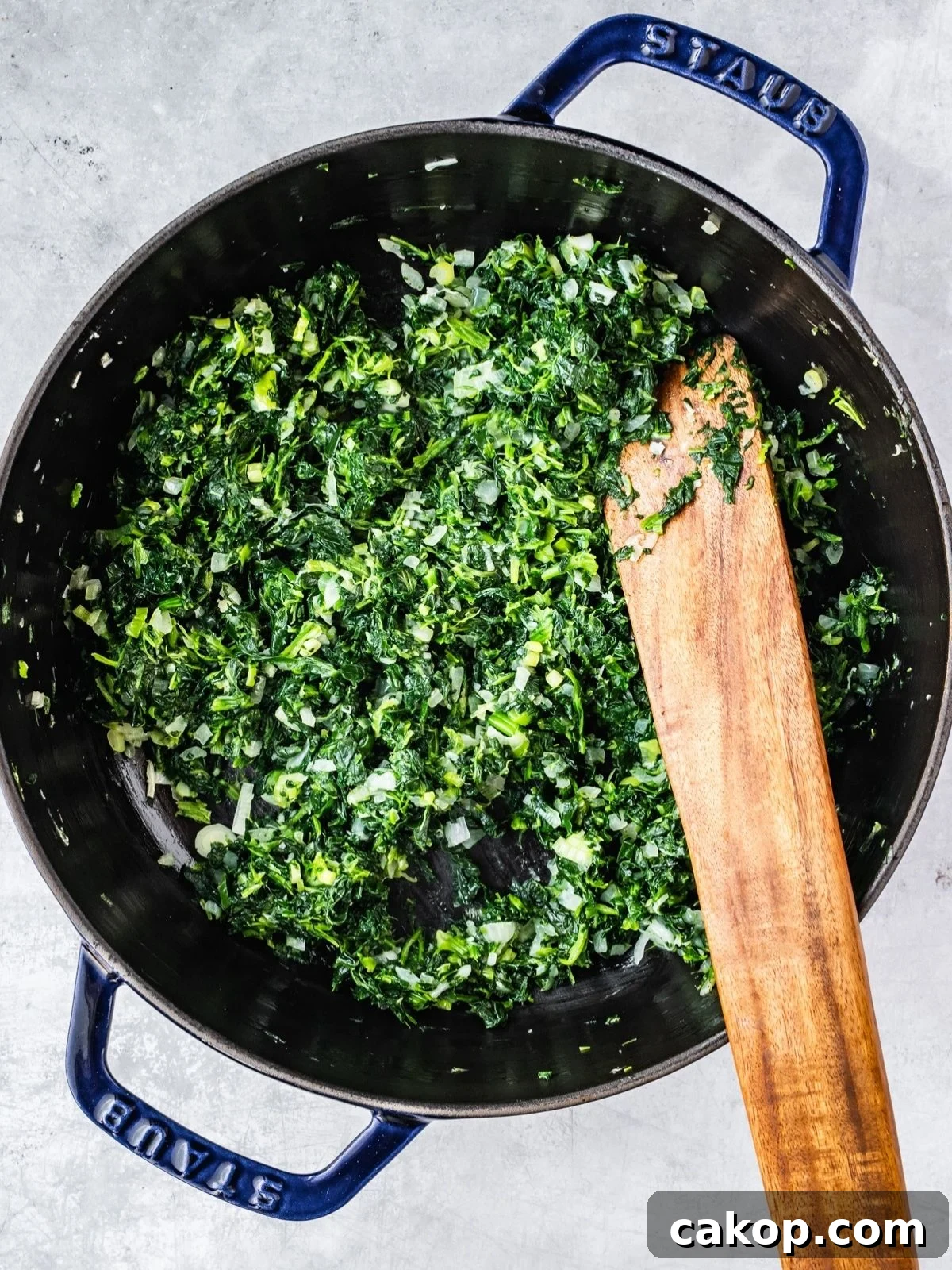 Adding the frozen and drained spinach to the pot with the fried onion.