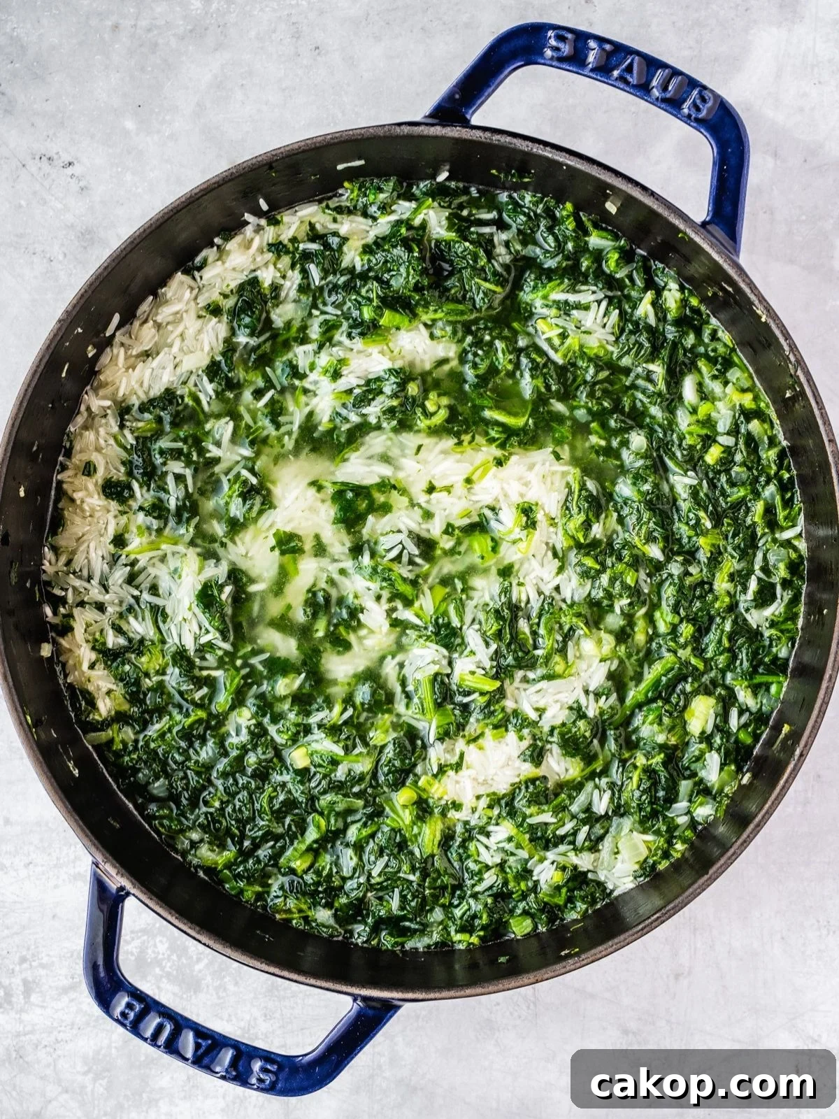 Adding the rice and water to the pot with the fried spinach and onion mixture.