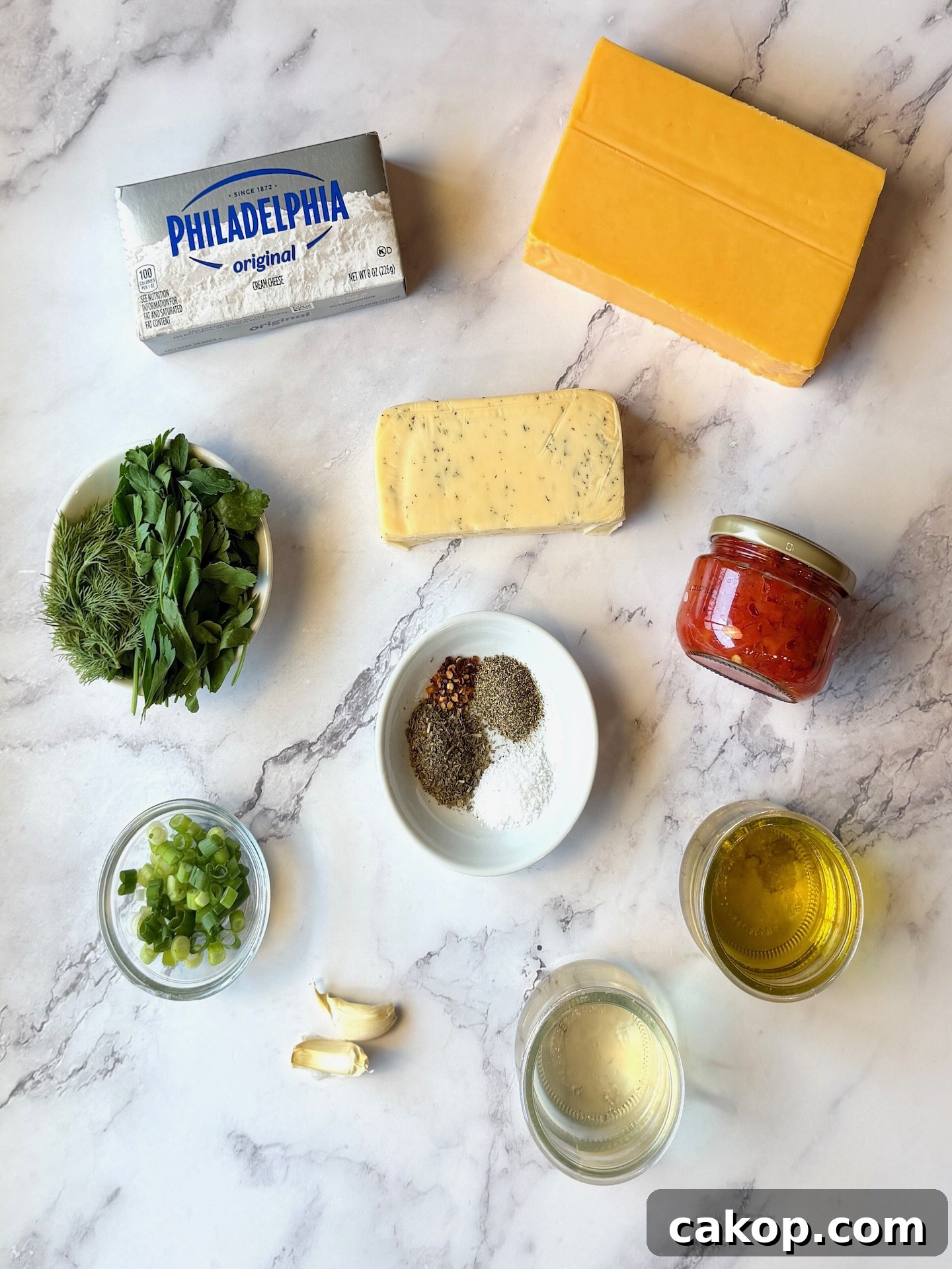 Mediterranean Marinated Cheese Bites for Party Appetizers 3 Ingredients displayed for marinated cheese. Cheddar cheese block, havarti cheese block, cream cheese block, jarred pimentos, fresh herbs, seasonings, garlic, olive oil, vinegar, and green onions.