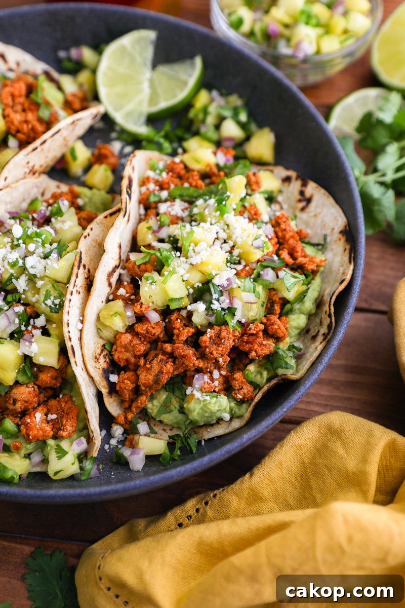 Ground pork al pastor tacos sitting in a large blue bowl topped with fresh pineapple salsa