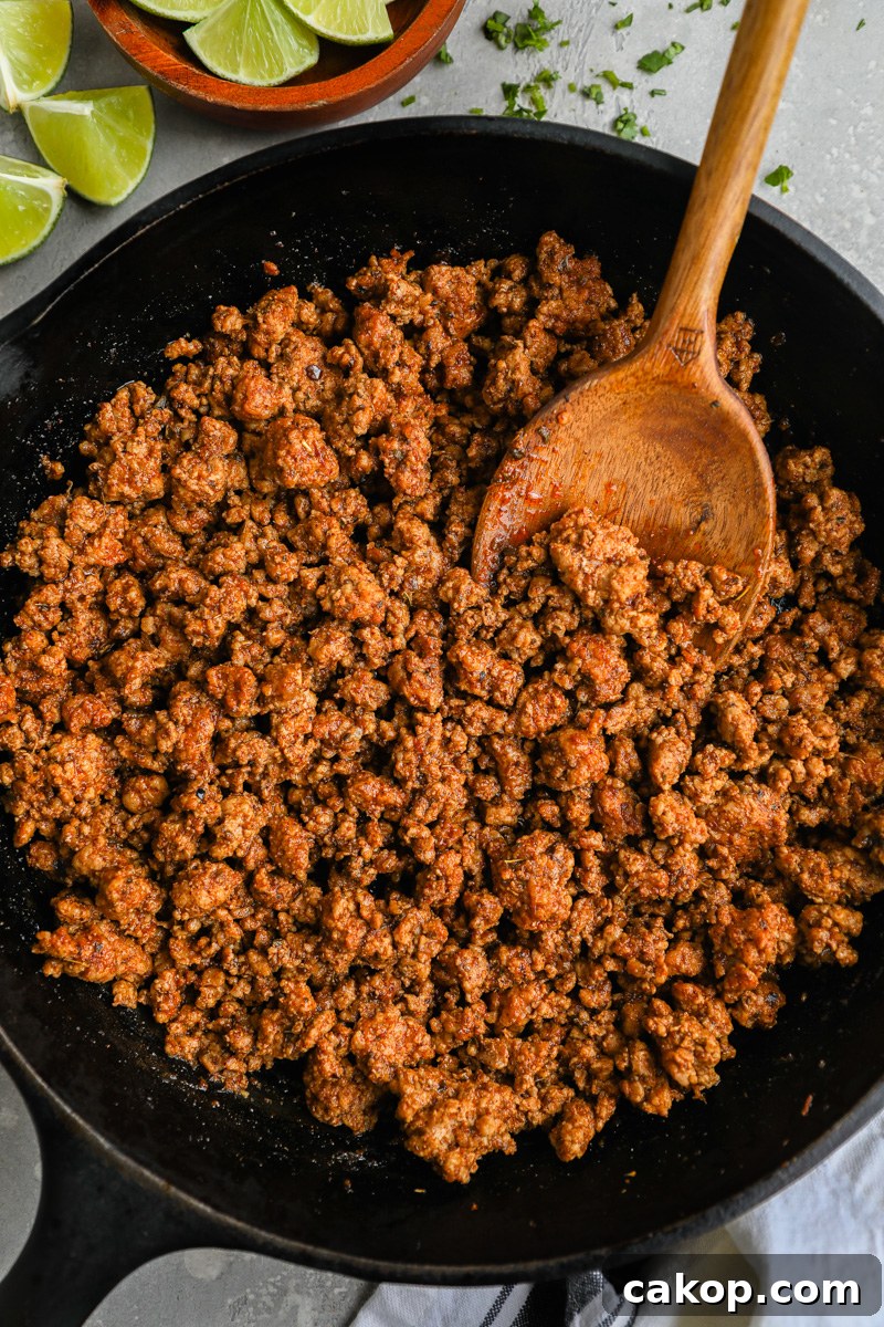 A large skillet filled with ground pork al pastor taco meat sitting next to a small bowl of limes