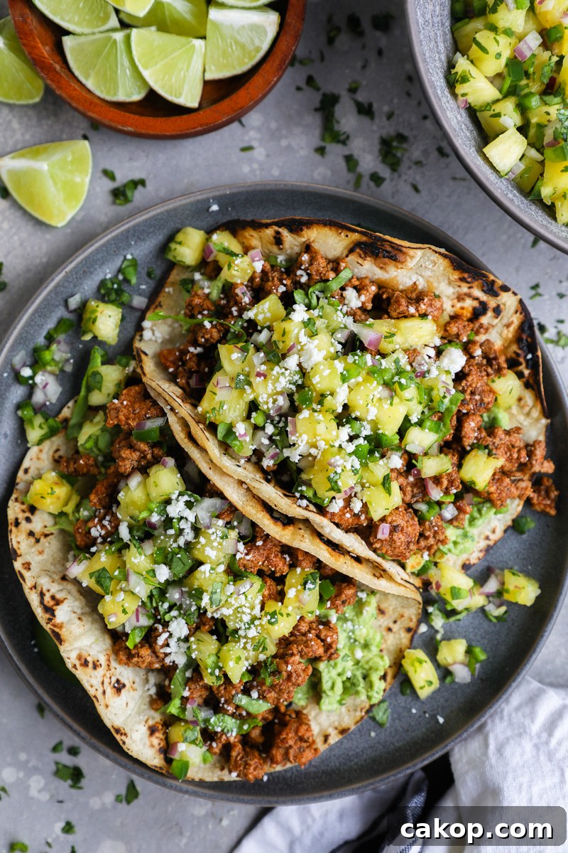 Ground pork al pastor tacos sitting on a large plate surrounded by fresh lime wedges and a bowl of pineapple salsa