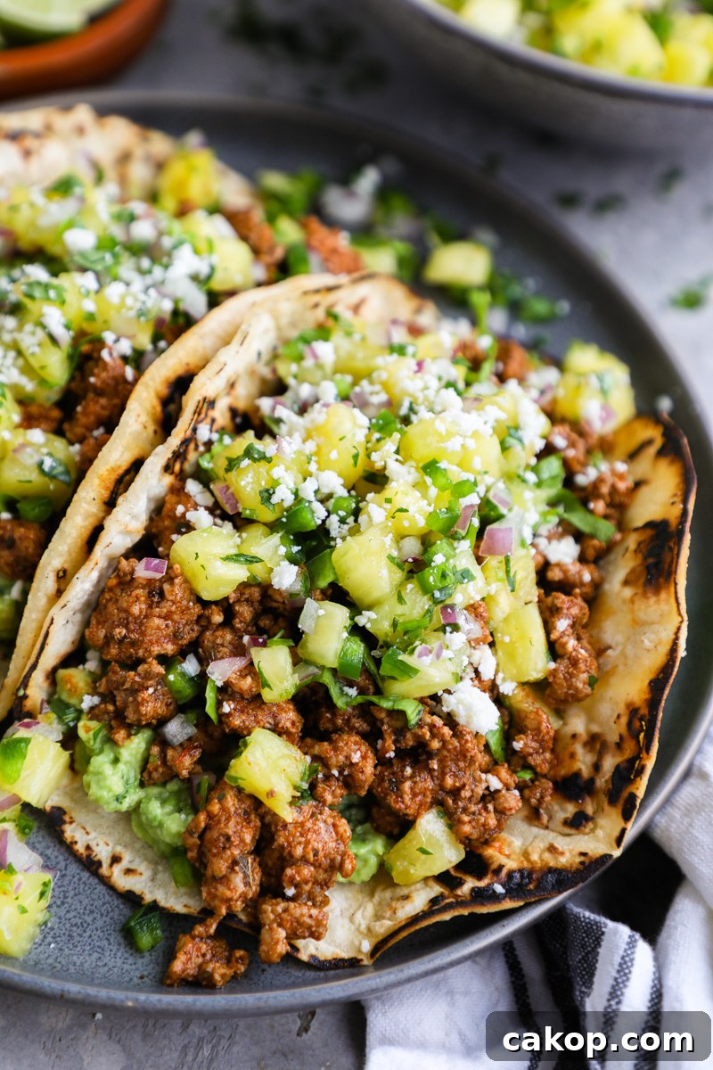 A close up photo of ground pork al pastor tacos topped with fresh pineapple salsa and cotija cheese