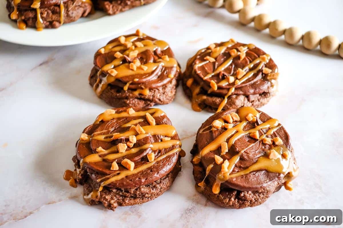 Chocolate Caramel Cookies with frosting, caramel drizzle, and chopped nuts on a white marble surface.