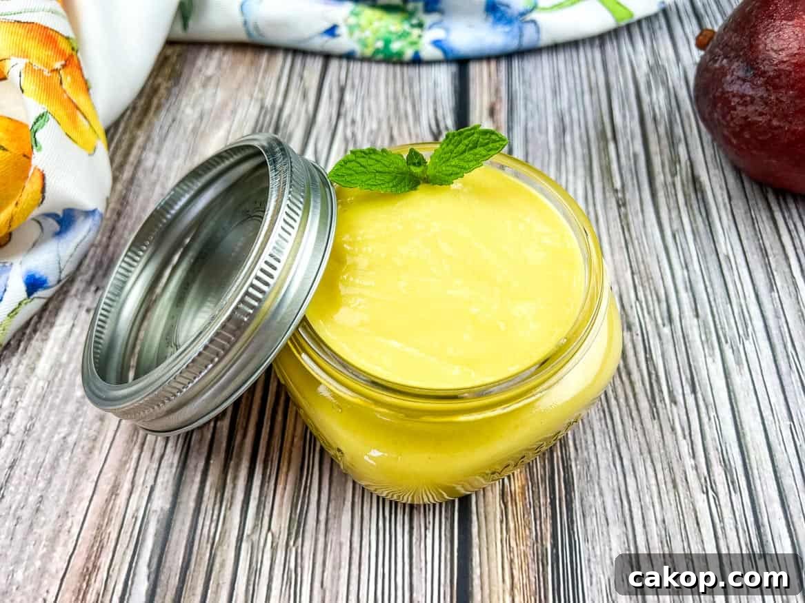 A jar of mango curd next to a mango and a mint leaf.