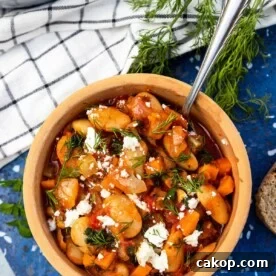 Greek Gigantes Plaki with Canned Giant Beans: Authentic Recipe 8 An overhead view of a ceramic dish of Greek giant beans with fresh herbs and feta crumbled on top, on a blue marble plate stand with slices of bread, fresh dill, a white and blue checked tea towel and a bigger pan of the beans around it.