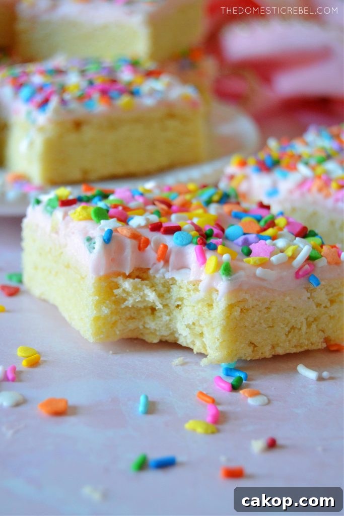 Sprinkle Sugar Cookie Bars Recipe — Soft, Chewy, Crowd-Pleasing 6 Sugar Cookie Bars with a bite missing on a pink board